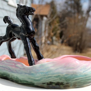 May include: A black ceramic horse figurine standing in a pink and green glazed ceramic planter.