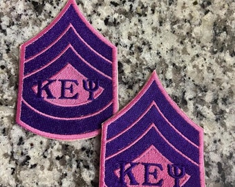 May include: Two purple and pink embroidered patches with the letters "KEY" and the Greek letter "Psi" in the center. The patches have a chevron design with three stripes.