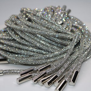 May include: A bundle of sparkling silver shoelaces, densely covered in shimmering rhinestones. The laces have silver metal aglets. The overall effect is glamorous and eye-catching, suitable for adding a touch of sparkle to footwear.