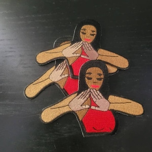 Könnte beinhalten: Drei gestickte Aufnäher mit einer Frau mit brauner Haut und schwarzen Haaren, die die 'OK'-Handgeste macht. Die Frau trägt ein rotes Kleid und hat einen braunen Umriss. Die Aufnäher sind übereinander gestapelt.
