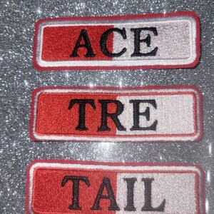 May include: Three red and white embroidered patches with black lettering. The patches read "ACE", "TRE", and "TAIL".