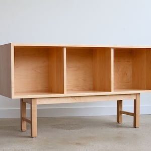 May include: A light wood bookcase with three open shelves and four legs. The bookcase is made of solid wood and has a simple, modern design.