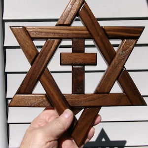 May include: A dark brown wooden Star of David with a centered wooden cross. The six-pointed star is constructed from interlocking wooden beams, and a small cross is positioned in the middle of the star, creating a combined religious symbol.