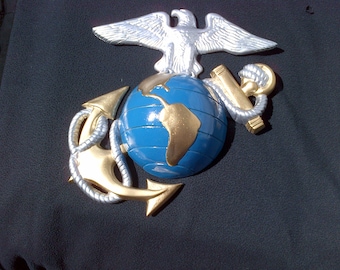 May include: A gold-colored anchor and globe with a silver eagle perched on top. The globe is blue with a gold-colored continent. This is a decorative wall hanging.
