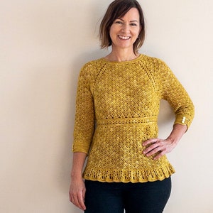 Könnte beinhalten: Ein gelber Häkelpullover mit Rundhalsausschnitt und 3/4-Ärmeln. Der Pullover hat ein zartes Muster und einen Rüschen-Saum.