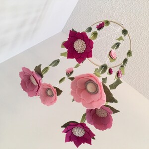 May include: A pink and white felt flower mobile with a wooden ring. The mobile features multiple flowers with different sizes and shapes.