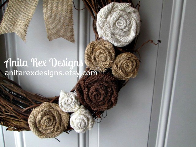 May include: A brown twig wreath decorated with burlap flowers in shades of brown, beige, and white. The wreath is accented with burlap bows and the text "Anita Rex Designs anitarexdesigns.etsy.com".