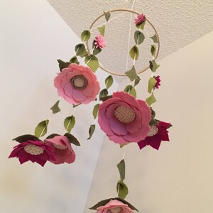 May include: A pink and green felt flower mobile with a wooden hoop. The mobile features multiple pink flowers with green leaves hanging from the hoop.