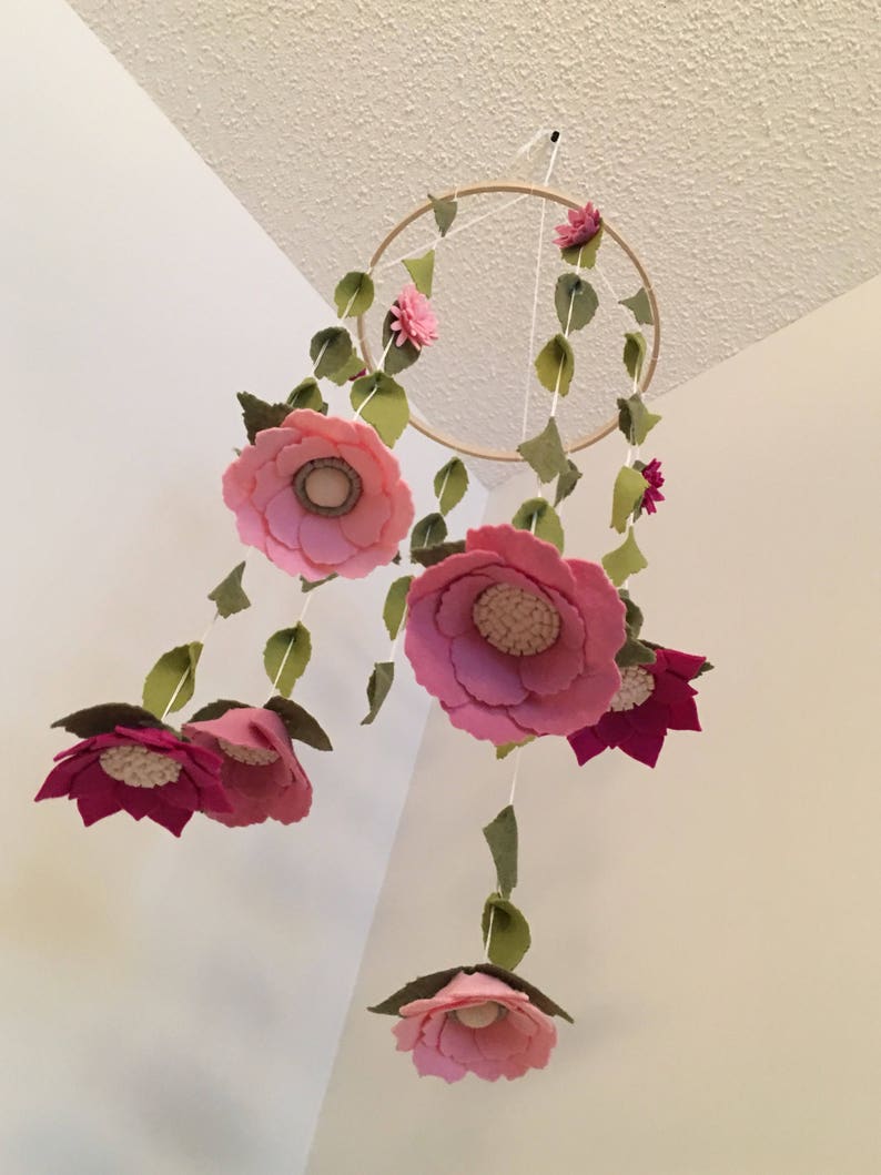 May include: A pink and green felt flower mobile with a wooden hoop. The mobile features multiple pink flowers with green leaves hanging from the hoop.