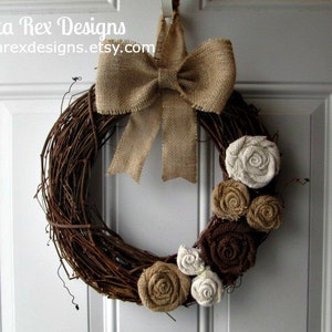 May include: A brown grapevine wreath decorated with burlap bows and fabric flowers in shades of brown, beige, and white. The wreath is hanging on a white door.