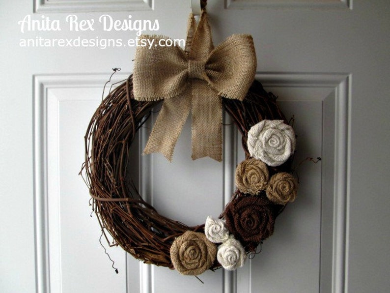 May include: A brown grapevine wreath decorated with burlap bows and fabric flowers in shades of brown, beige, and white. The wreath is hanging on a white door.