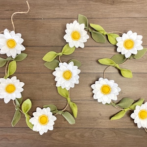 May include: A felt garland with white daisies and green leaves. The garland is strung together with twine.