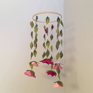 May include: A wooden ring mobile with pink felt flowers and green felt leaves hanging from it.
