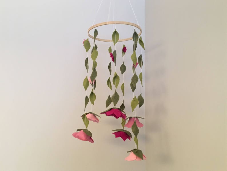 May include: A wooden ring mobile with pink felt flowers and green felt leaves hanging from it.