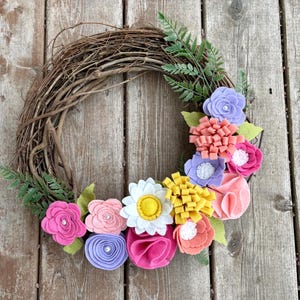 Corona de flores de fieltro para primavera y verano en tonos rosa, melocotón, lila y amarillo.