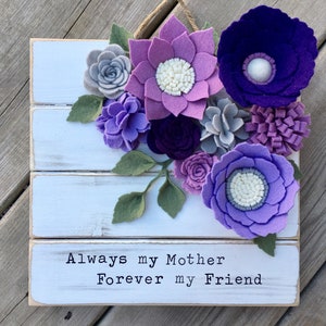 May include: A white wooden sign with a purple, lavender, and gray felt flower arrangement. The sign reads "Always my Mother Forever my Friend".