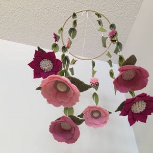 May include: A pink and purple felt flower mobile with green felt leaves hanging from a wooden ring.