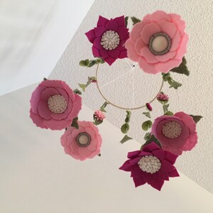 May include: A pink and magenta felt flower mobile with a circular metal frame. The mobile features six flowers with white centers and green felt leaves.