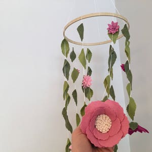 May include: A pink felt flower mobile with green felt leaves hanging from a wooden hoop. The mobile is made of felt and is a great addition to a nursery or child's room.