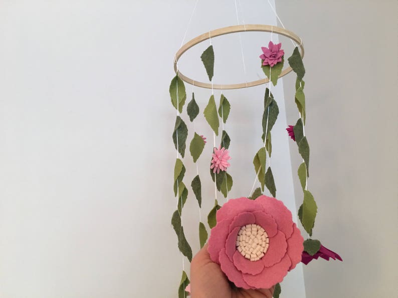 May include: A pink felt flower mobile with green felt leaves hanging from a wooden hoop. The mobile is made of felt and is a great addition to a nursery or child's room.