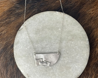 The “Adrian” necklace of a half circle with three rectangles layered up on a bib style necklace focal point