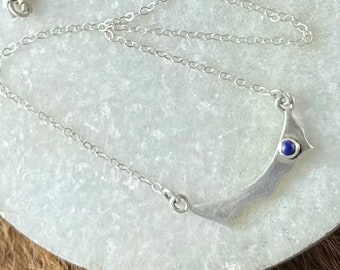 Ingrid necklace, an irregular swooping sterling silver metal shape with small lapis lazuli stone