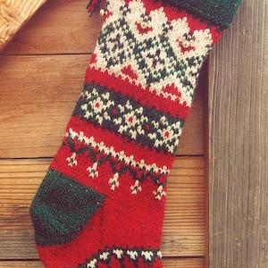 Könnte beinhalten: Ein rot-grün-weißer gestrickter Weihnachtsstrumpf mit Schneeflockenmuster, der an einer Holzoberfläche hängt.