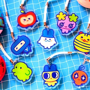 Puede incluir: Colección de coloridos colgantes acrílicos con personajes de dibujos animados y un juego portátil retro. Los colgantes incluyen una manzana, una abeja, un conejito y otros diseños bonitos. Cada colgante tiene un cordón blanco adjunto.