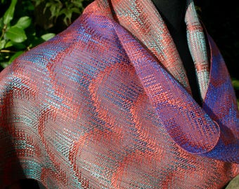 May include: A woven scarf in shades of red, blue, and purple. The fabric has a textured appearance with a wave-like pattern. The scarf is draped, showcasing the color variations and intricate weave.