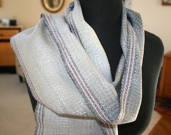 May include: A gray and white woven scarf with red stripes. The scarf is draped over a mannequin's neck.