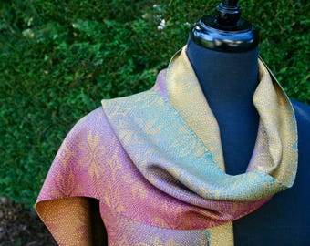 May include: A colorful woven scarf with a gradient of purple, blue, and gold. The scarf is draped over a mannequin's neck.