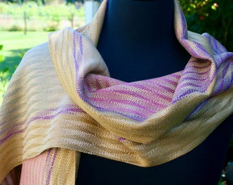 May include: A woven scarf in shades of beige, pink, and purple with a herringbone pattern.