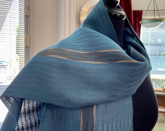 May include: A teal woven scarf featuring a subtle chevron texture and horizontal stripes in dark blue and metallic gold. The fabric displays a consistent weave pattern throughout, with the stripes running parallel along the length of the material.