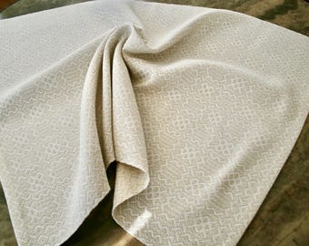 May include: A white linen throw blanket with a subtle geometric pattern. The blanket is folded and draped over a wooden surface.