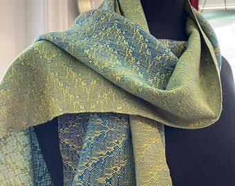 May include: A woven scarf featuring a complex, repeating pattern in shades of lime green and deep blue. The fabric displays a textured, interlaced design where the two colors alternate to create a dense, intricate visual effect across the entire surface.