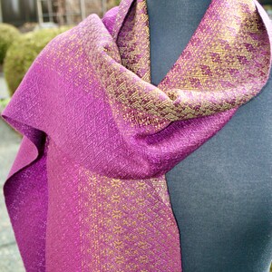 Pode incluir: Um cachecol de seda roxo e dourado com um padr&atilde;o geom&eacute;trico. O cachecol est&aacute; drapeado sobre um manequim.