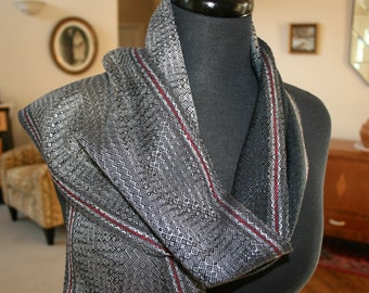 May include: A black and white patterned scarf with red stripes. The scarf is made of a soft, woven fabric and is draped over a black mannequin.