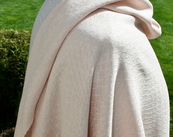 May include: A soft, pale pink woven shawl with a subtle diamond pattern. The shawl is draped over a mannequin and appears to be made of a lightweight fabric.