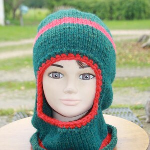 Peut inclure: Un bonnet en tricot vert avec une bordure rouge et un tour de cou assorti. Le bonnet a un rabat qui peut être tiré vers le bas pour couvrir les oreilles et le cou.