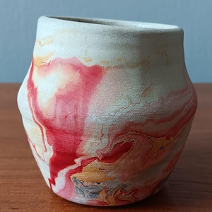 May include: A white ceramic pot with red and yellow marbling. The pot has a rounded shape and a smooth, textured surface.
