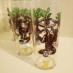 May include: Set of four clear glass drinking glasses with a green and brown monkey design. Each glass has a different monkey and the text "See No Evil", "Speak No Evil", and "Hear No Evil".