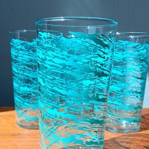 May include: Three clear glass tumblers with a turquoise blue abstract design. The design is made up of thin lines and dots.