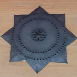 May include: A dark blue, star-shaped metal ornament with a circular cutout in the center. The ornament is decorated with a pattern of small holes.