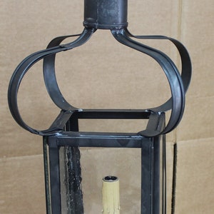 May include: A black metal hanging lantern with clear glass panels. The lantern has a decorative crown-like top and a candle holder inside. The lantern is designed with a vintage aesthetic and is suspended by a hook.