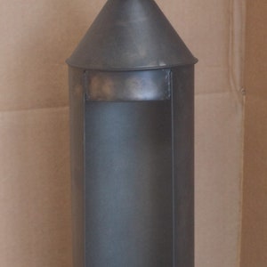 May include: A black metal candle lantern with a circular handle and a cone-shaped top. The lantern has a single candle holder.