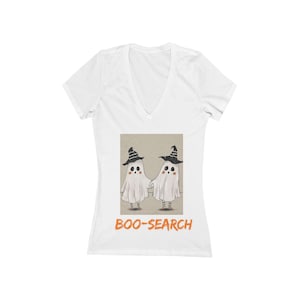 May include: A white V-neck t-shirt featuring a graphic of two ghosts wearing black witch hats and striped socks. The ghosts are holding hands, and the text "BOO-SEARCH" is printed in orange letters underneath the illustration on the front.
