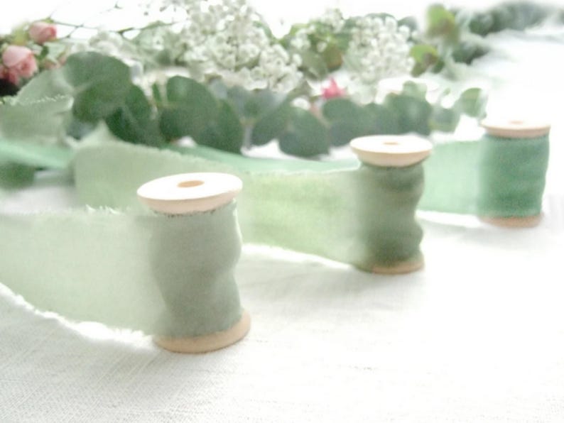Naturally dyed green silk ribbons in 3 tones: sage green, olive green and emerald green. Presented on wooden spool in the middle of green foliage and roses.Naturally hand dyed by Idy of Dyeing2meetU in France.