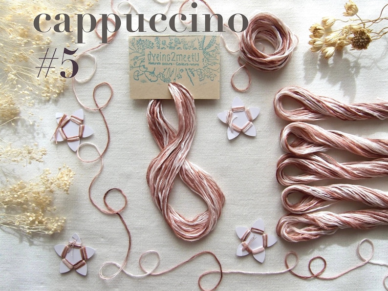 Fils à broder couleur cappuccino, composé de fils beige, rose et bruns. L'image présente des bobines, des écheveaux et des brins de fil lâches, ainsi que des décorations en forme d'étoile et une petite carte avec "Dyeing2meetU"