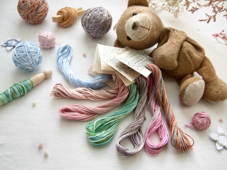 Fil de coton à broder de teinture végétale avec variation, 1 échevette de 8 m (8.7 yd) mouliné 6 brins, teint à la main en France. Divers coloris rose, bleu, vert, parme. Présenté par un petit ours sur un fond de lin blanc. Fait en France par Dyeing2meetU