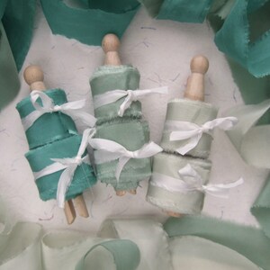 May include: Three spools of teal and green silk ribbon with frayed edges, tied with white ribbon and wooden spools.
